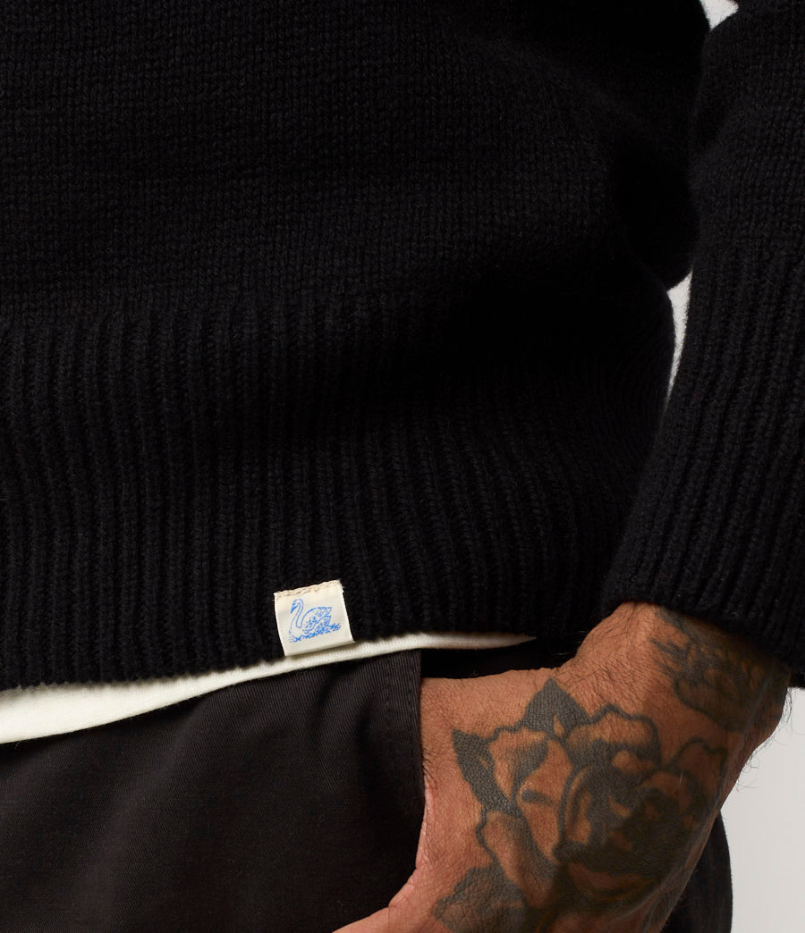 Black sweater with a brand label on a neutral background