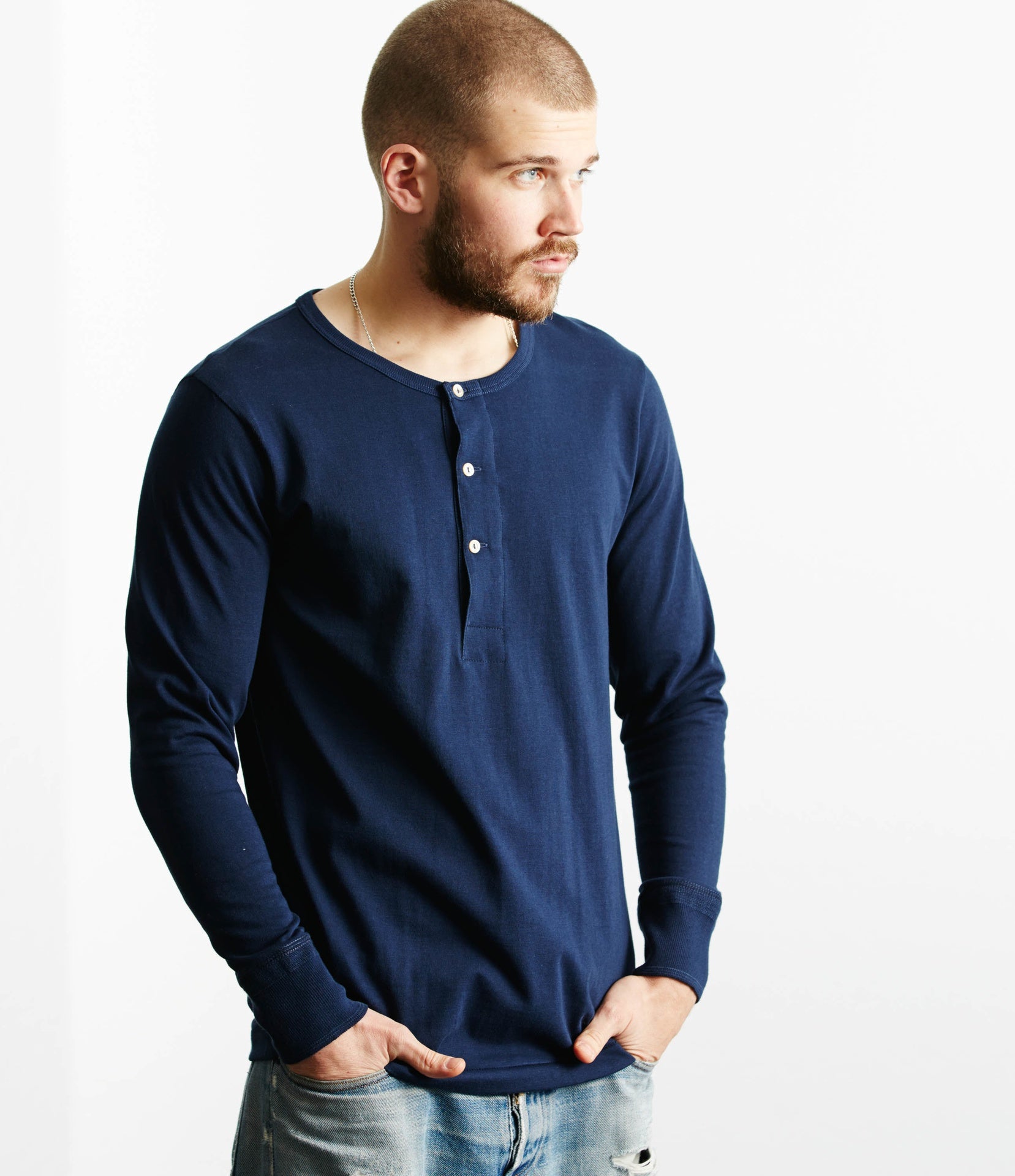 A man wearing a blue long sleeve henley shirt with buttons at the neck area, paired with light blue jeans.