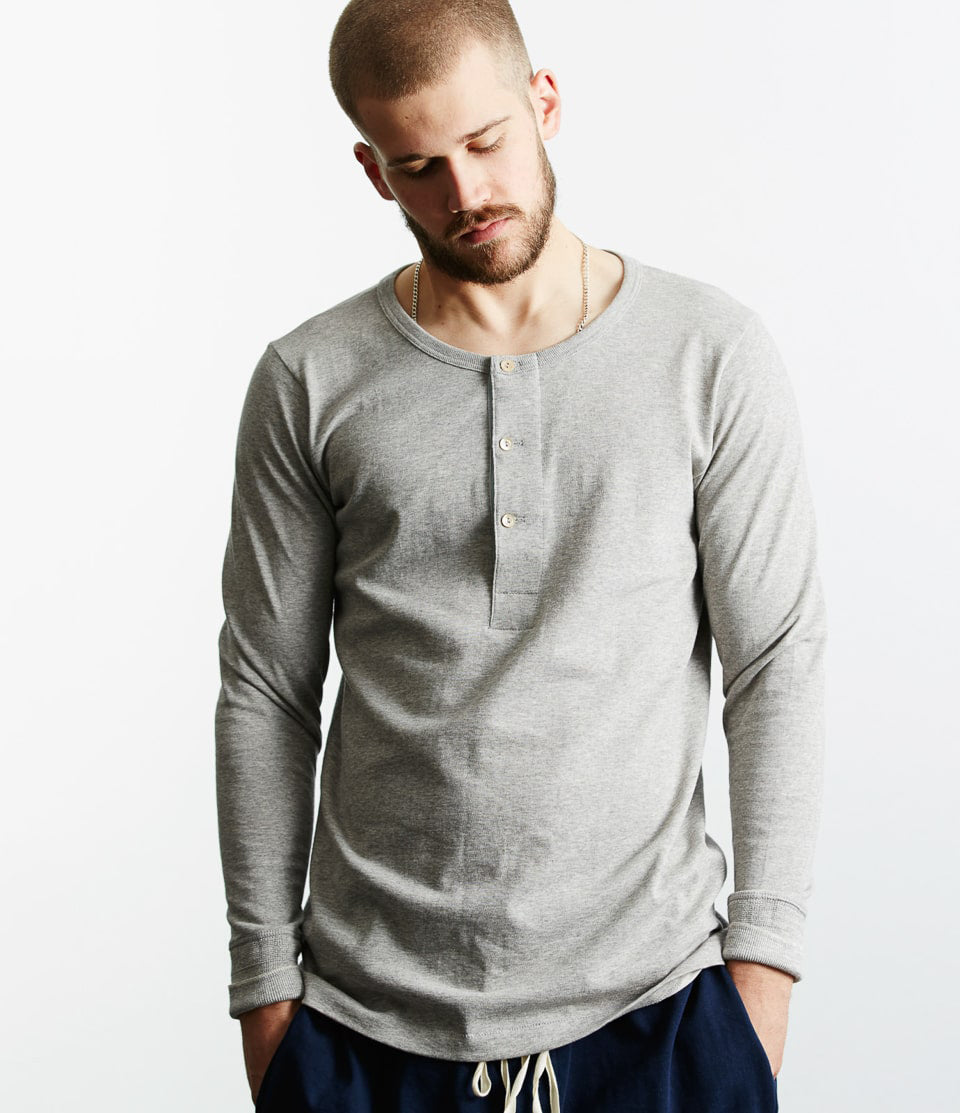 A male model wearing a gray long sleeve henley shirt with buttons at the neck and a relaxed fit.