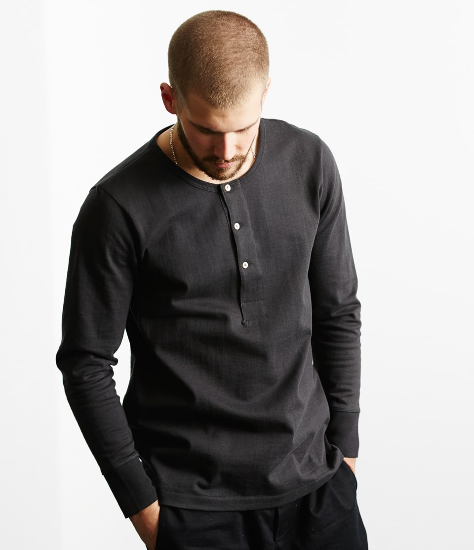 A male model wearing a long sleeve black henley shirt with a classic fit.