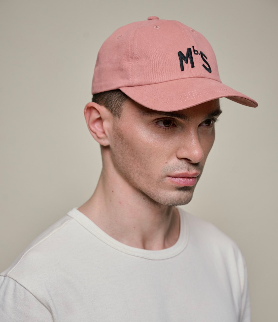 Man wearing a pink cap with 'Mbs' logo against a plain background