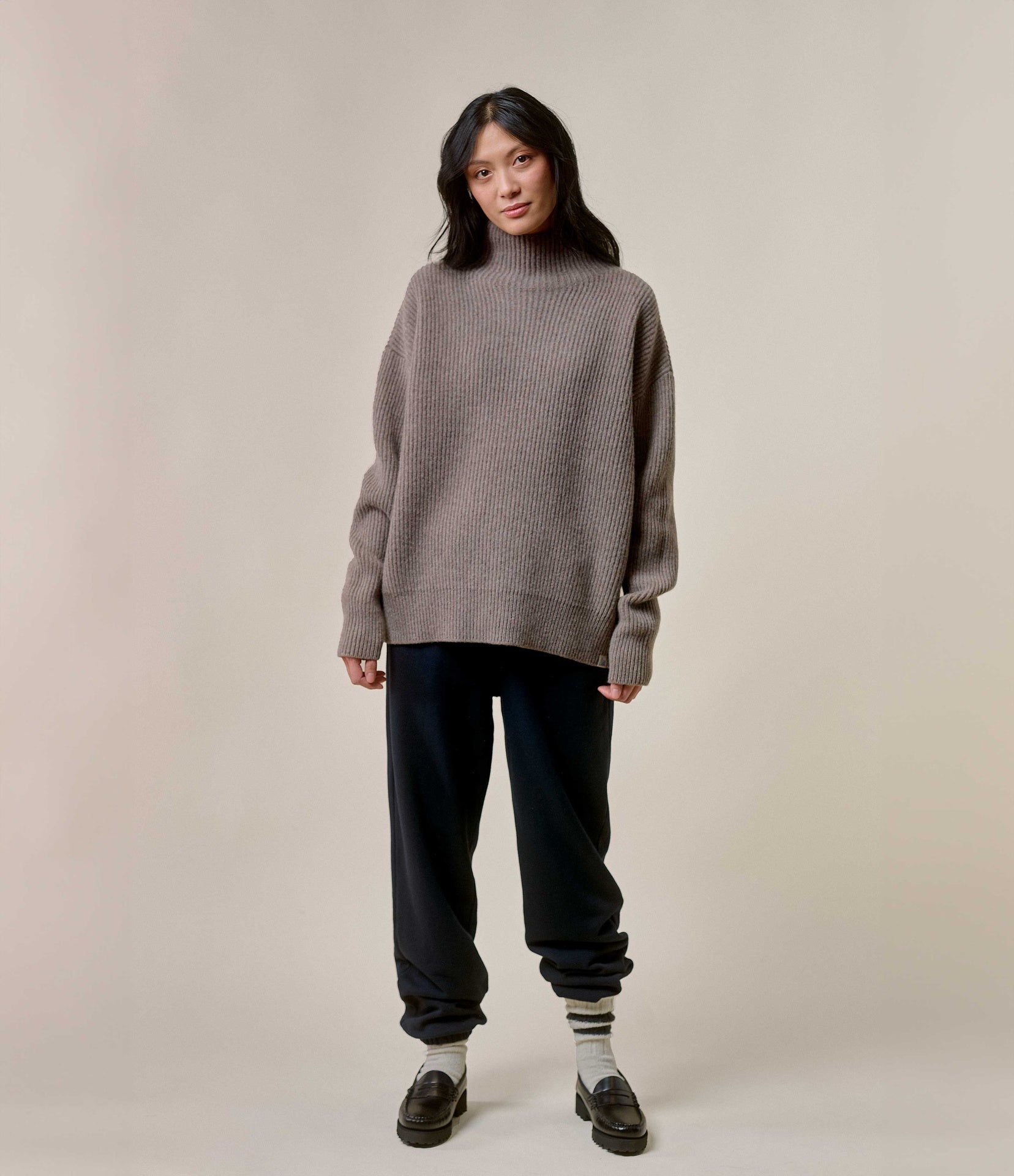 Person wearing a gray sweater and black pants against a plain background