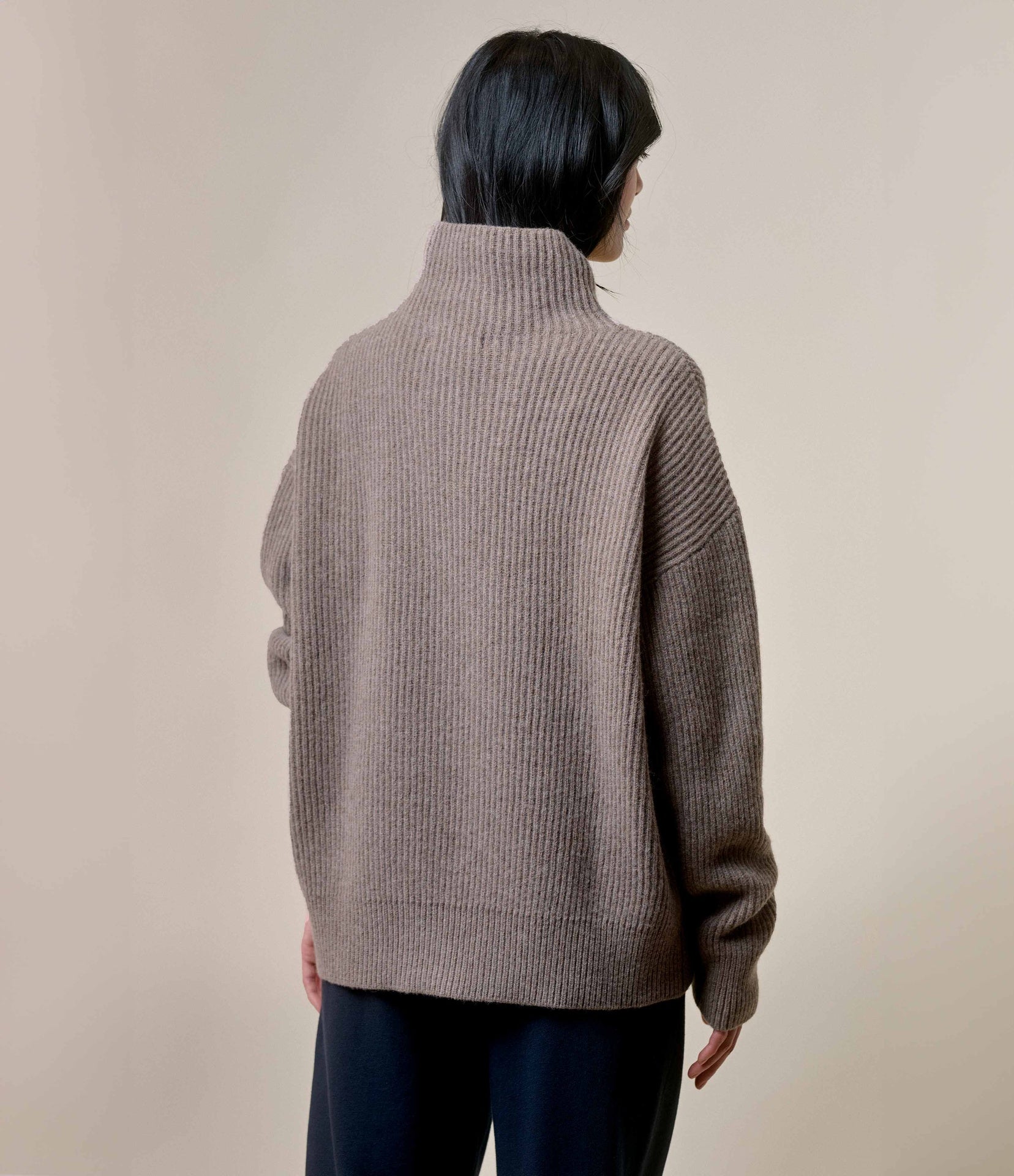 Person wearing a brown ribbed sweater against a plain background