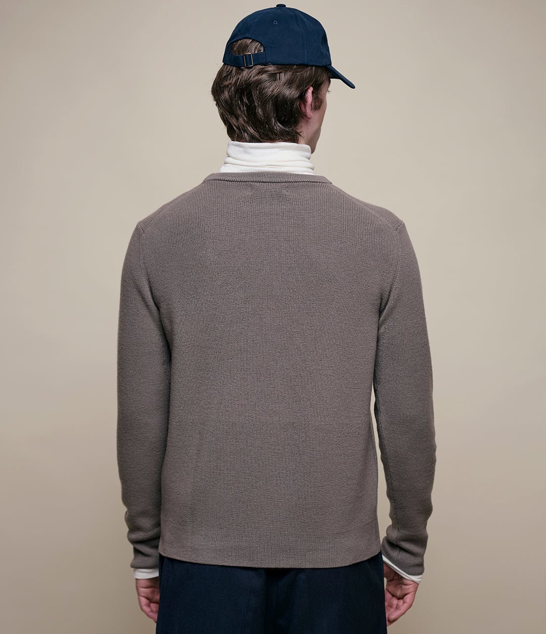 Person wearing a gray sweater and navy cap on a beige background