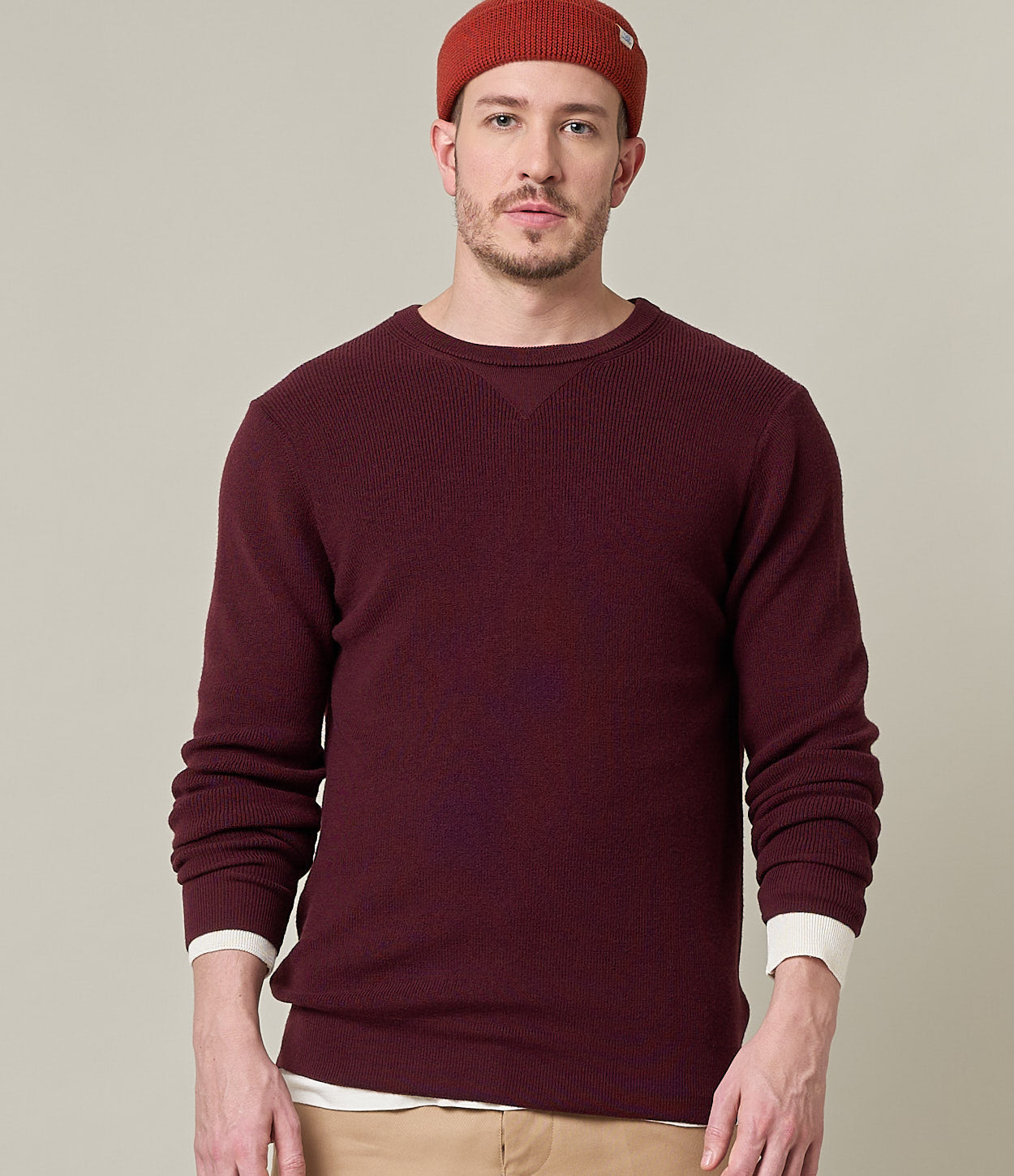 Man wearing a burgundy sweater and red beanie against a beige background