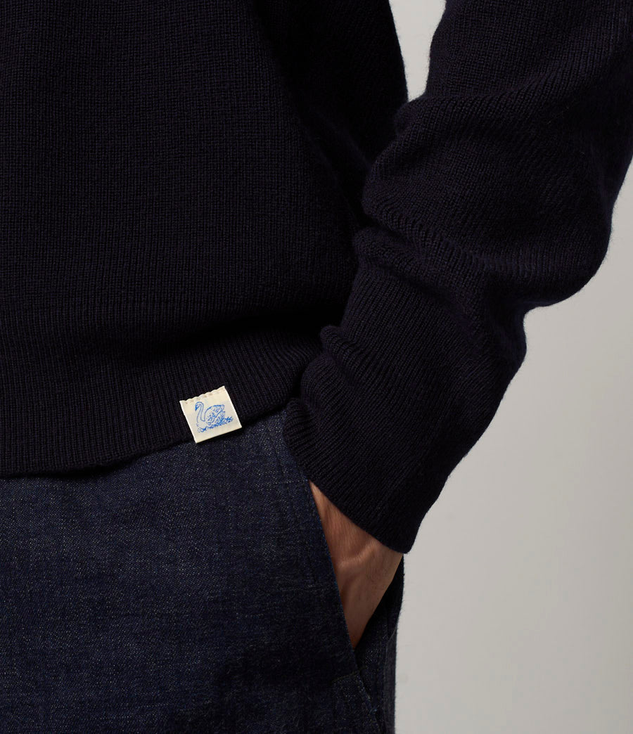 Person wearing a dark blue sweater with a visible brand label on a light gray background