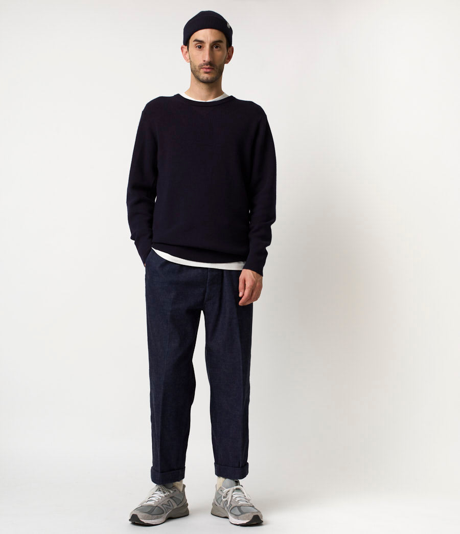 Man wearing a black sweater, dark pants, and gray shoes on a white background
