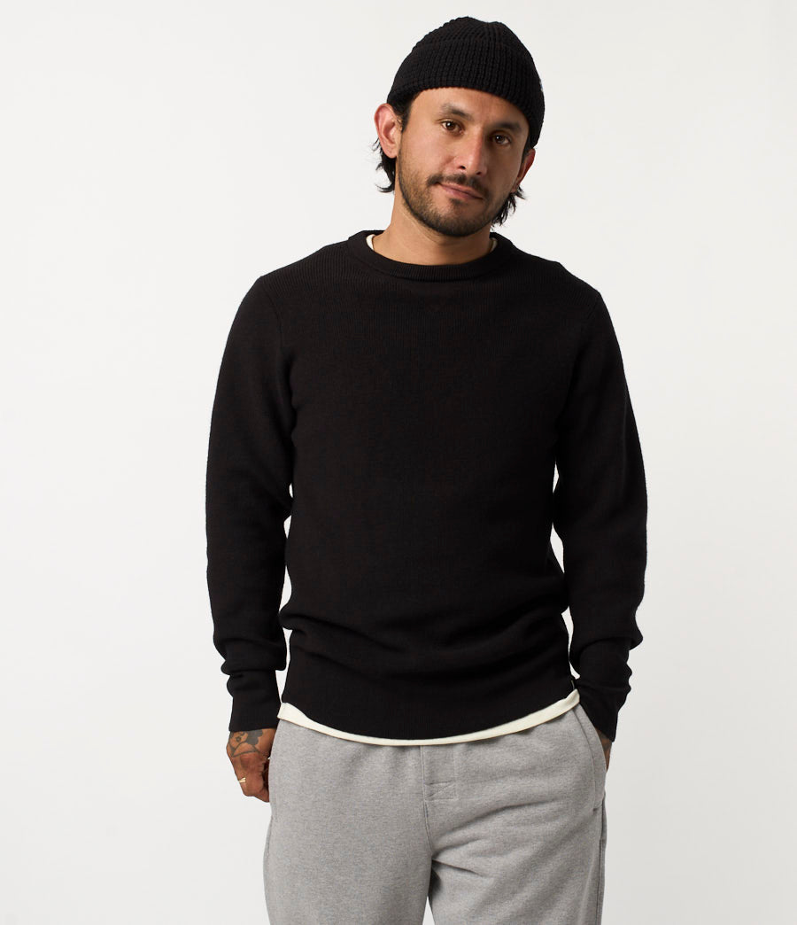 Man wearing a black sweater and gray pants on a white background