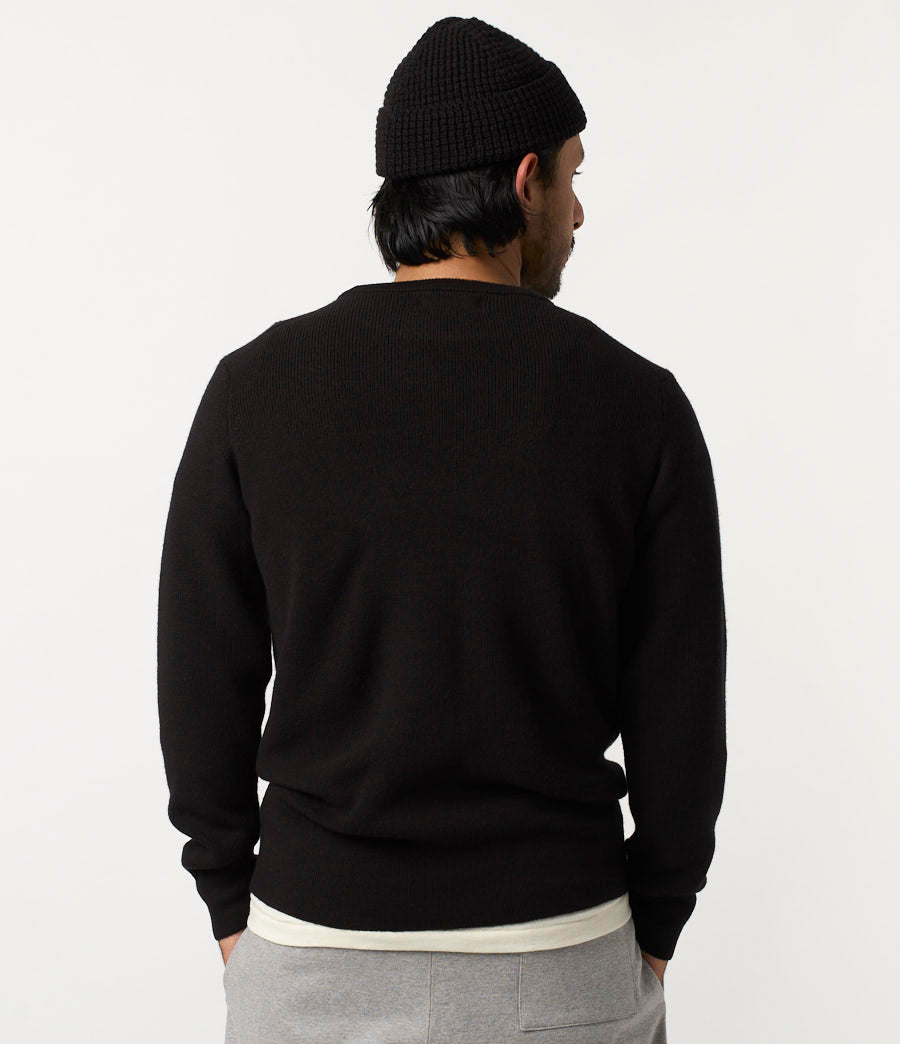 Person wearing a black sweater and beanie from behind on a light gray background