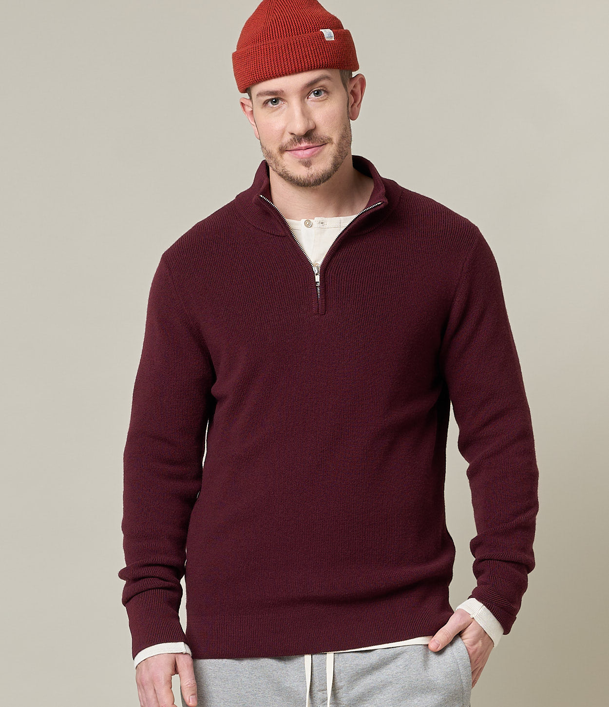Man wearing a burgundy sweater and red beanie against a beige background