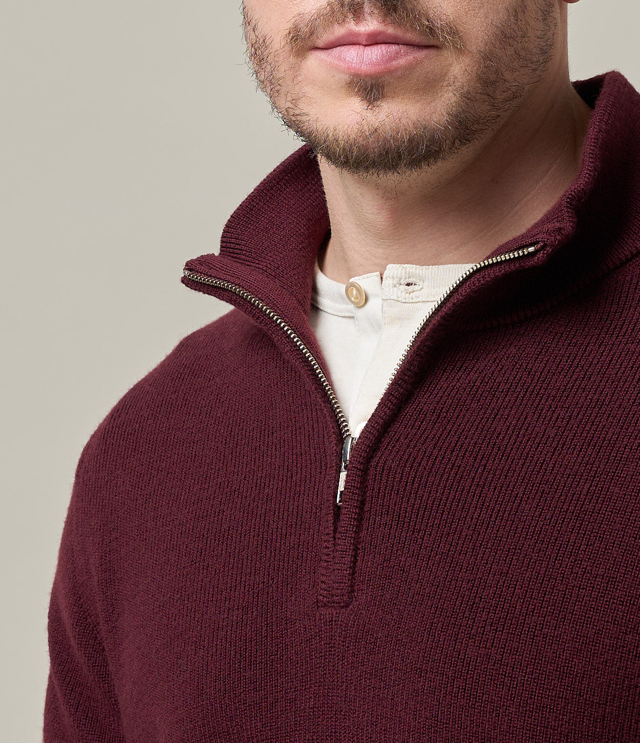 Man wearing a burgundy half-zip sweater over a beige shirt on a neutral background