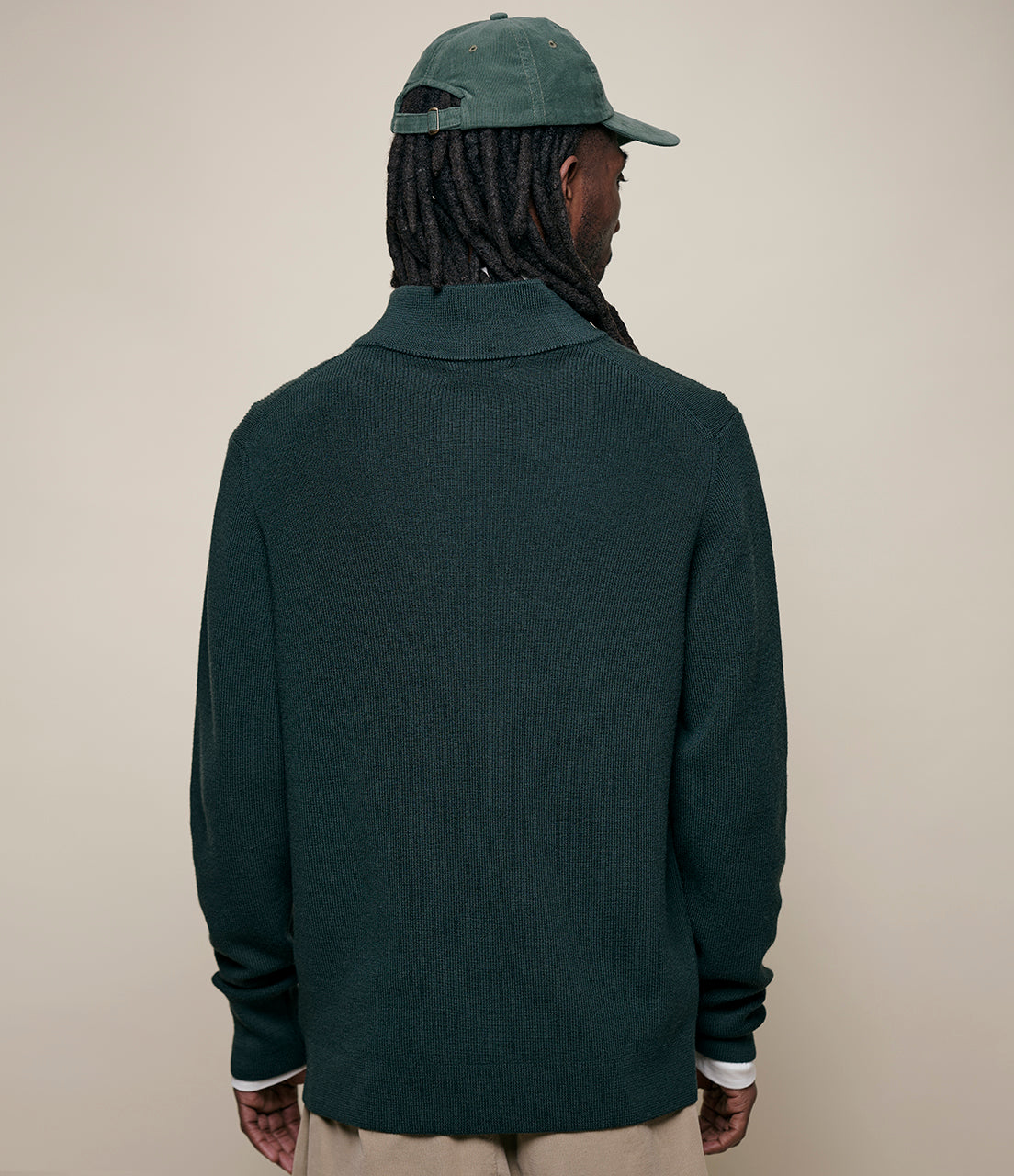 Person wearing a dark green sweater and cap on a beige background