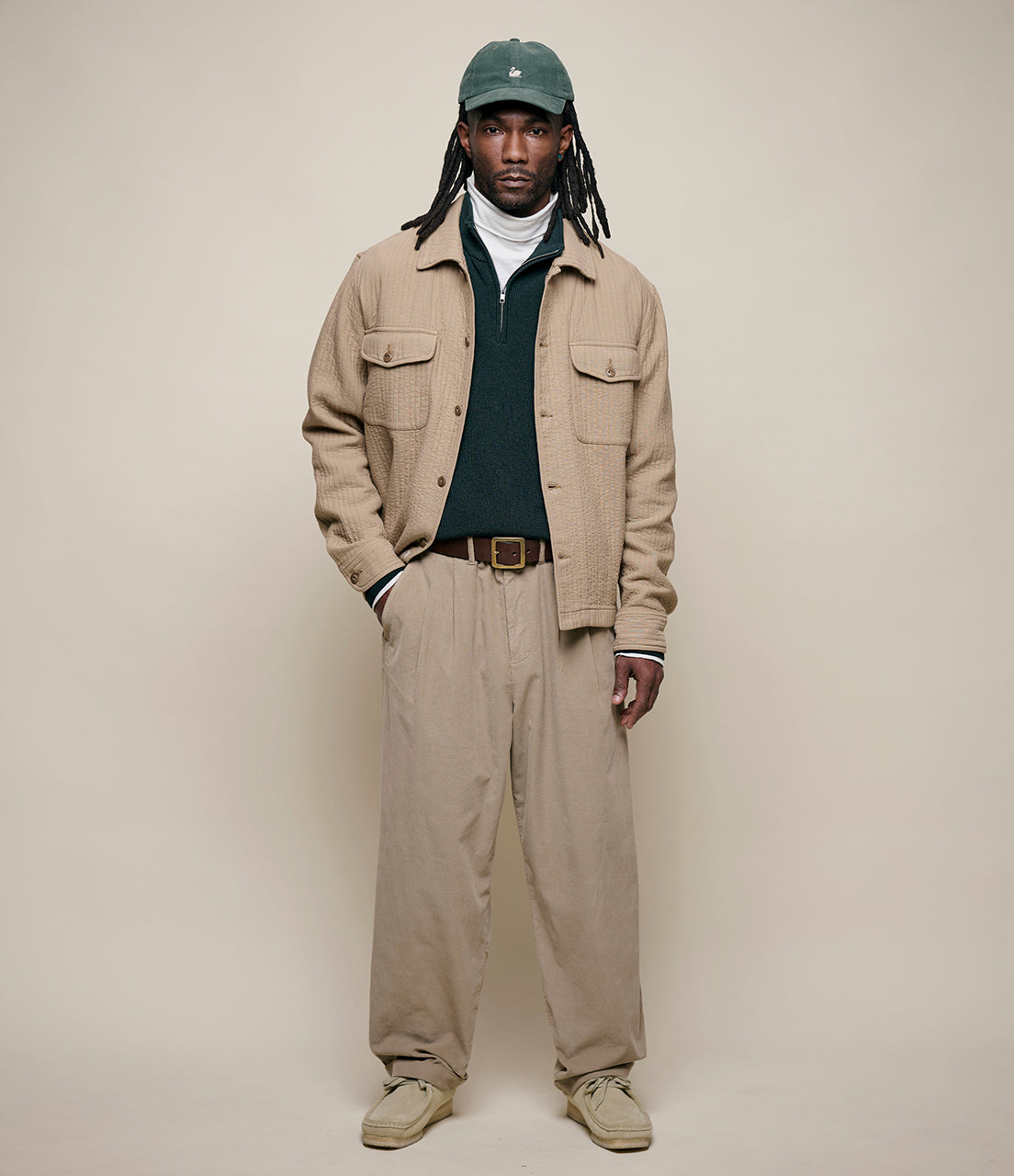 Person wearing a beige jacket, pants, and cap against a plain background