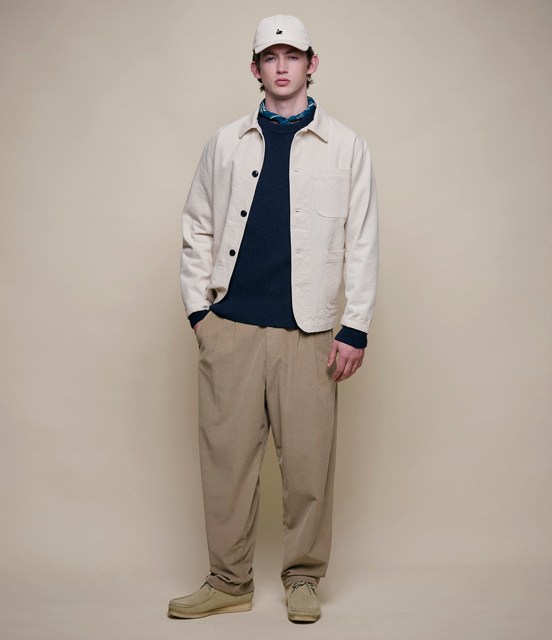 Man wearing a beige jacket, navy shirt, and beige pants against a plain background