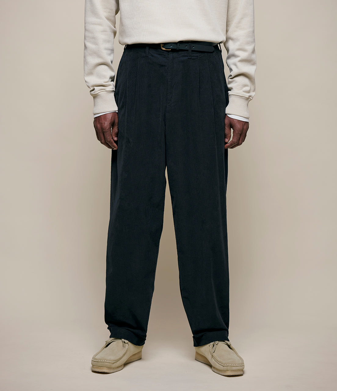 Person wearing black corduroy pants and a cream sweater on a beige background
