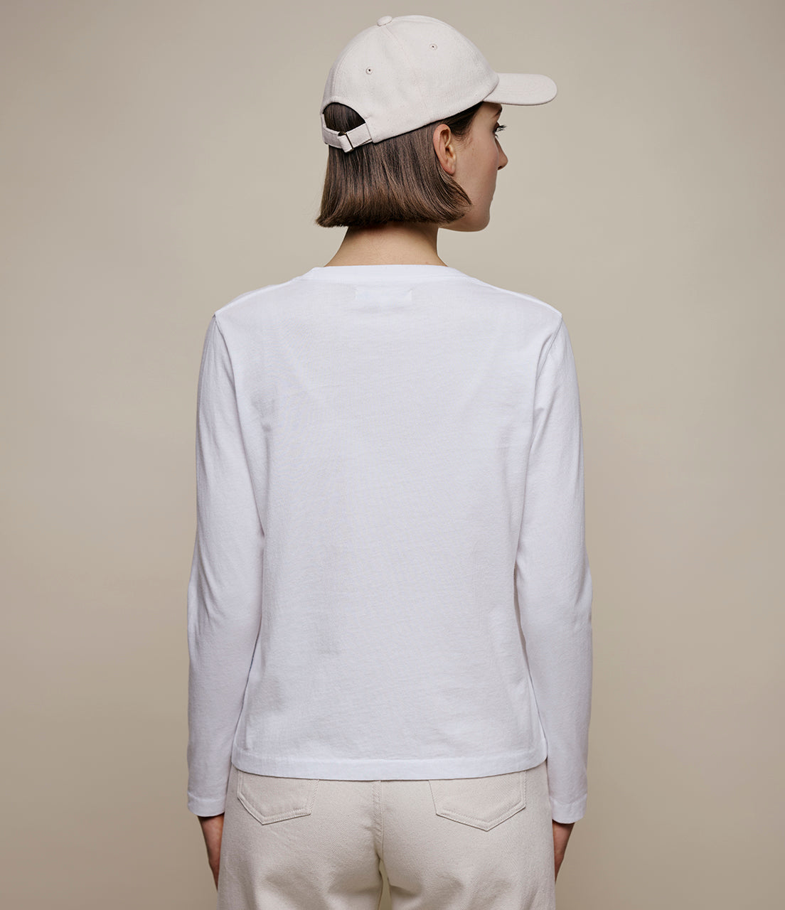 Person wearing a white long-sleeve shirt and beige cap on a plain background