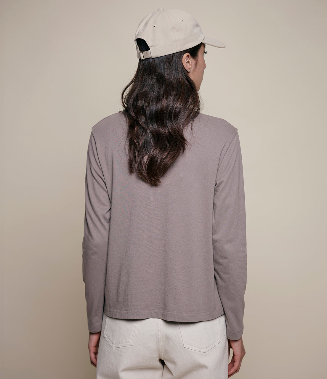 Person wearing a gray long-sleeve shirt and beige cap on a plain background