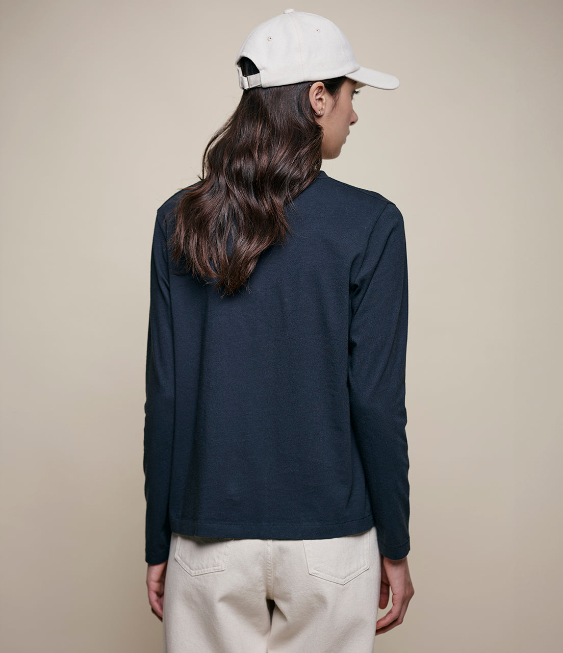 Person wearing a black long-sleeve shirt and beige pants against a beige background