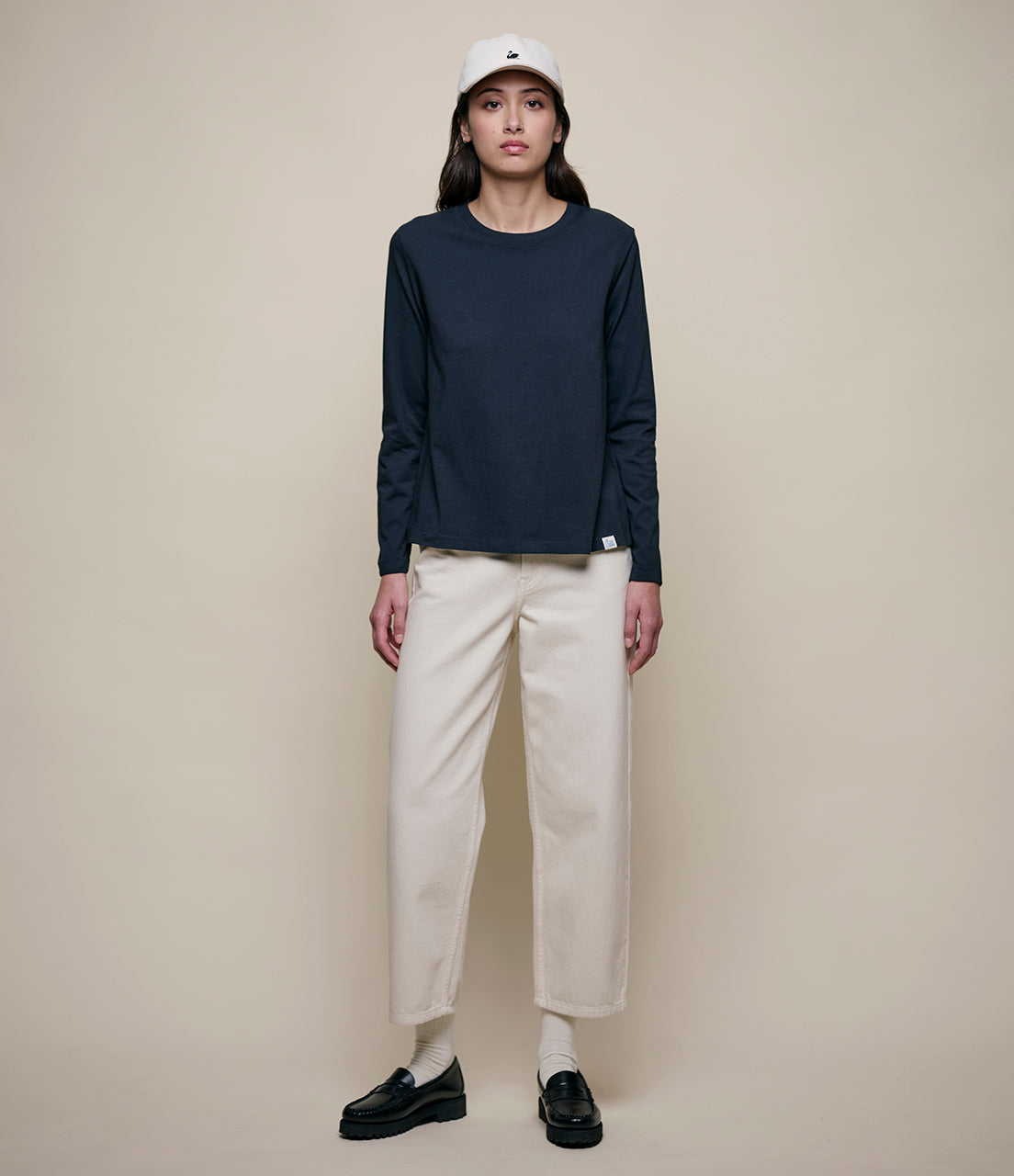 Person wearing a black long-sleeve shirt, beige pants, and black shoes on a beige background