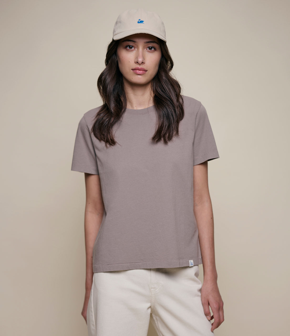 Woman wearing a gray t-shirt and beige cap against a plain background