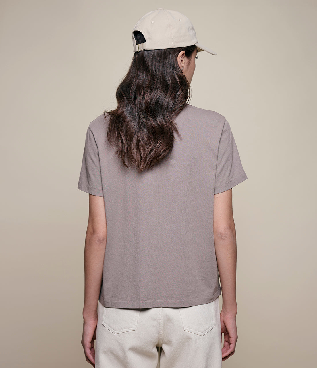 Person wearing a plain gray t-shirt and beige cap on a beige background
