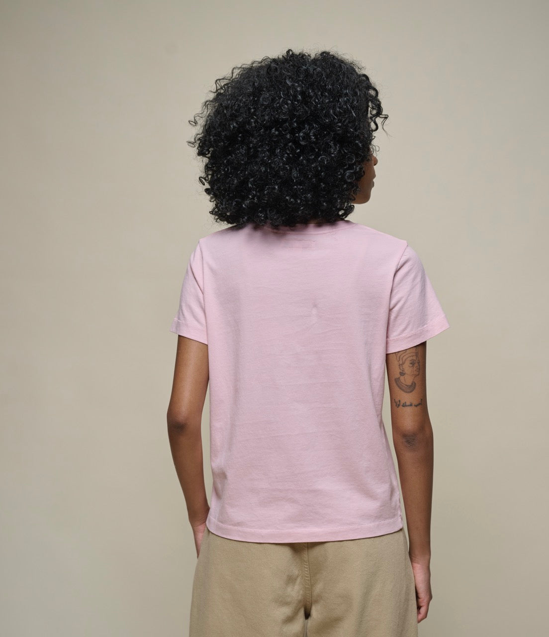 Person wearing a light pink t-shirt with a plain background