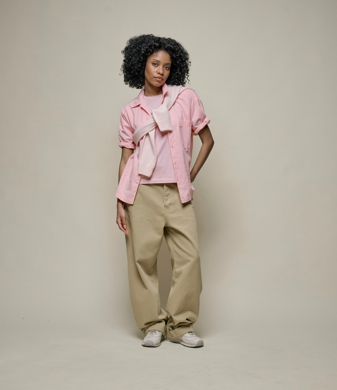 Person wearing a pink shirt and beige pants against a plain background