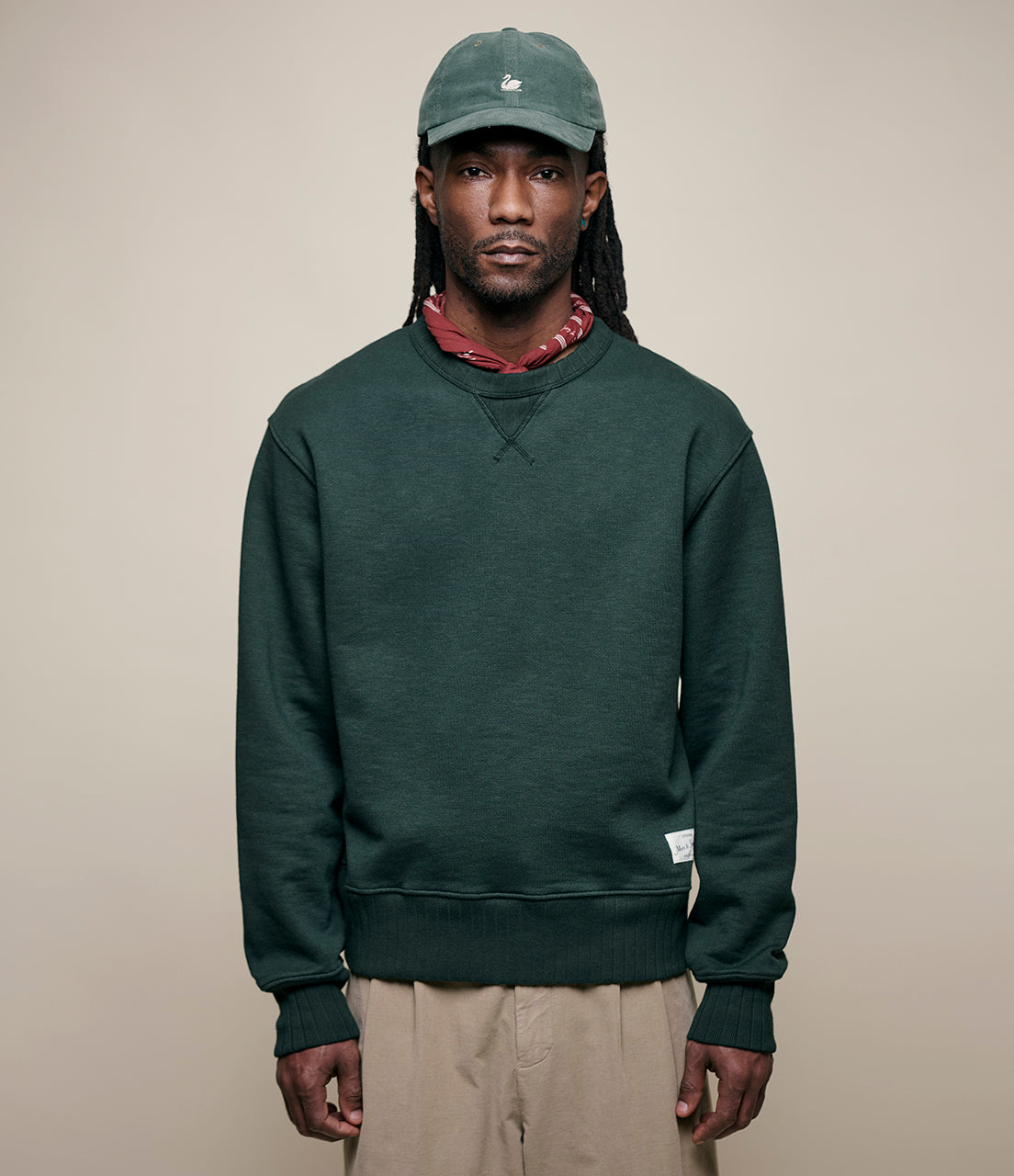 Man wearing a green sweatshirt and cap against a beige background