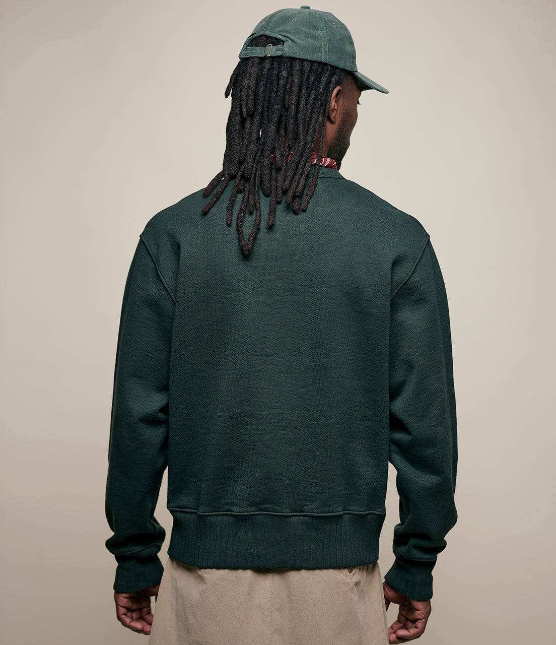 Person wearing a dark green sweatshirt and cap, facing away from the camera on a beige background