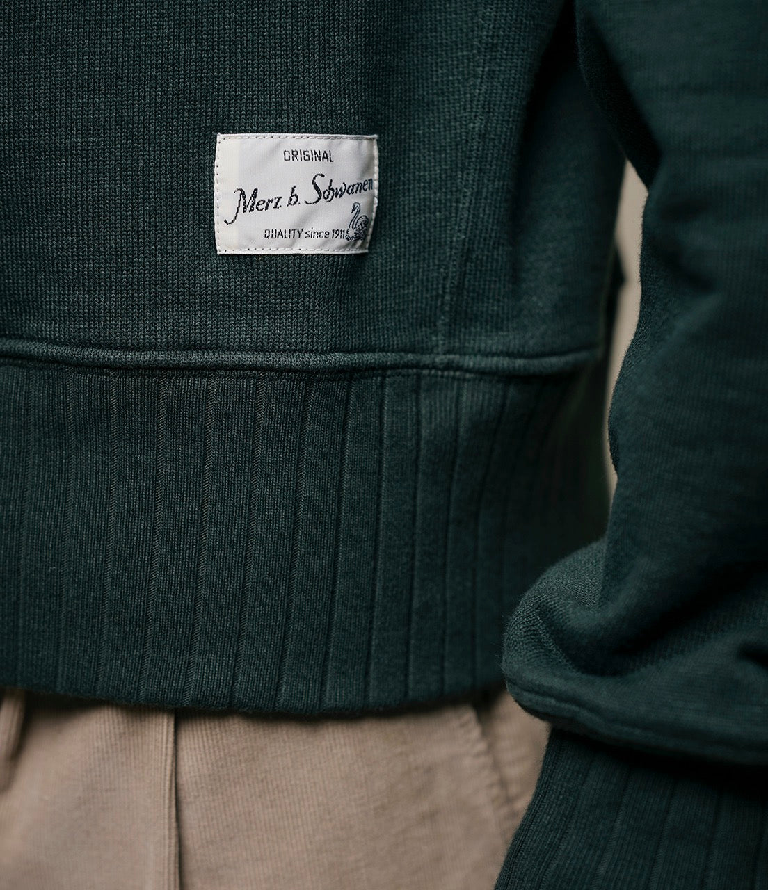 Dark green sweater with a brand label on a neutral background