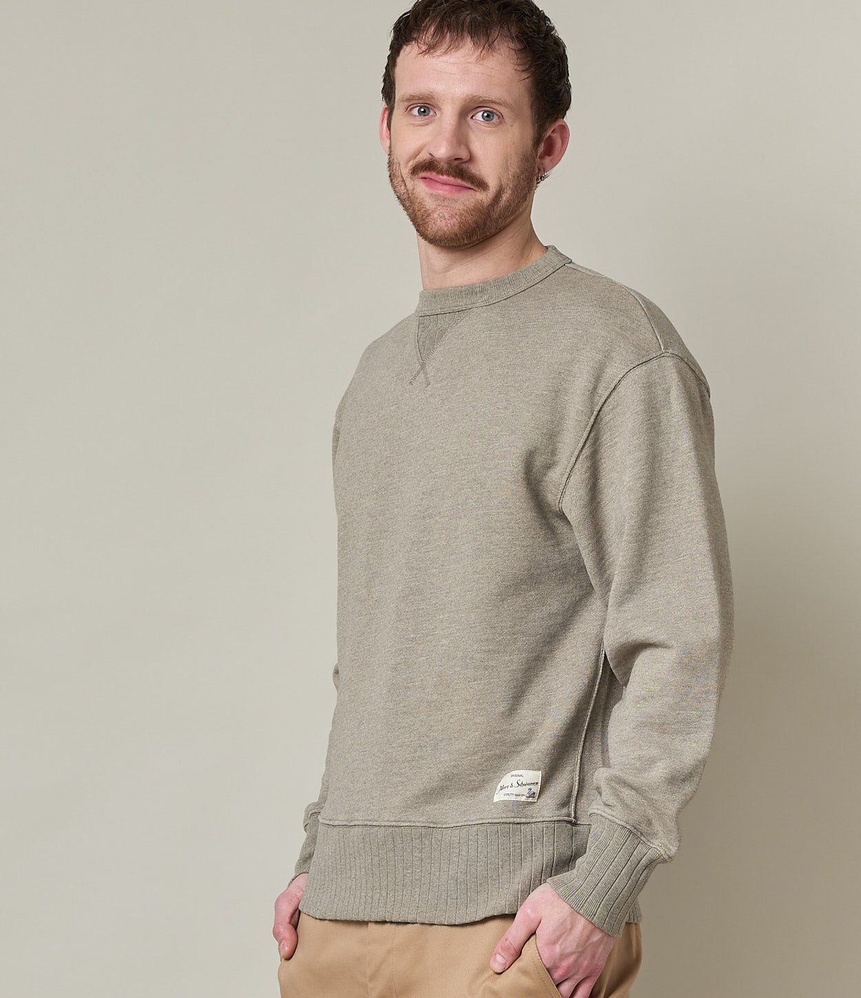 A male model wearing a grey, long-sleeved, round-neck fleece sweatshirt.