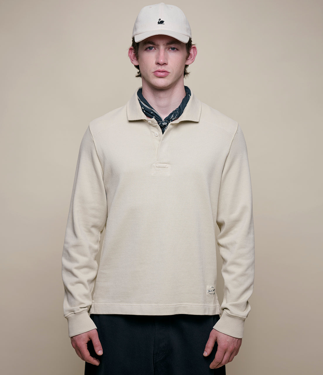 Person wearing a beige long-sleeve rugby shirt and white cap against a plain background