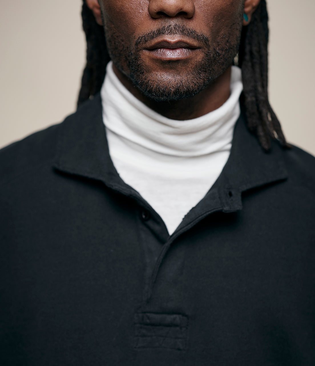 Man wearing a black rugby shirt over a white turtleneck against a neutral background