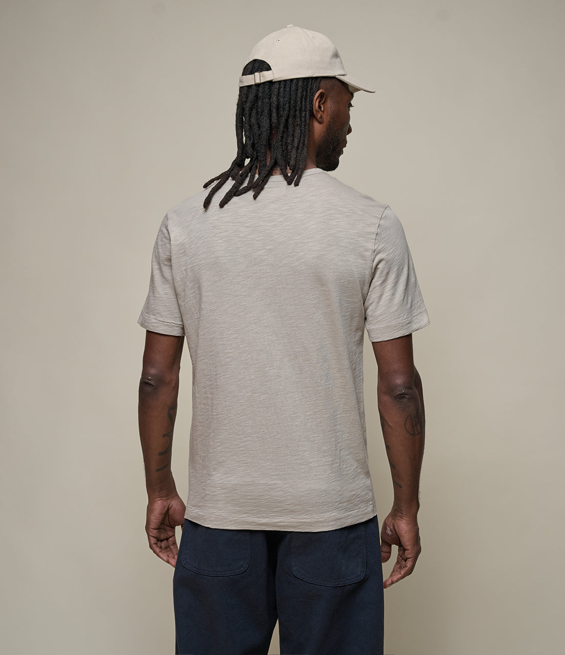 Man wearing a beige t-shirt and cap, facing away from the camera on a plain background