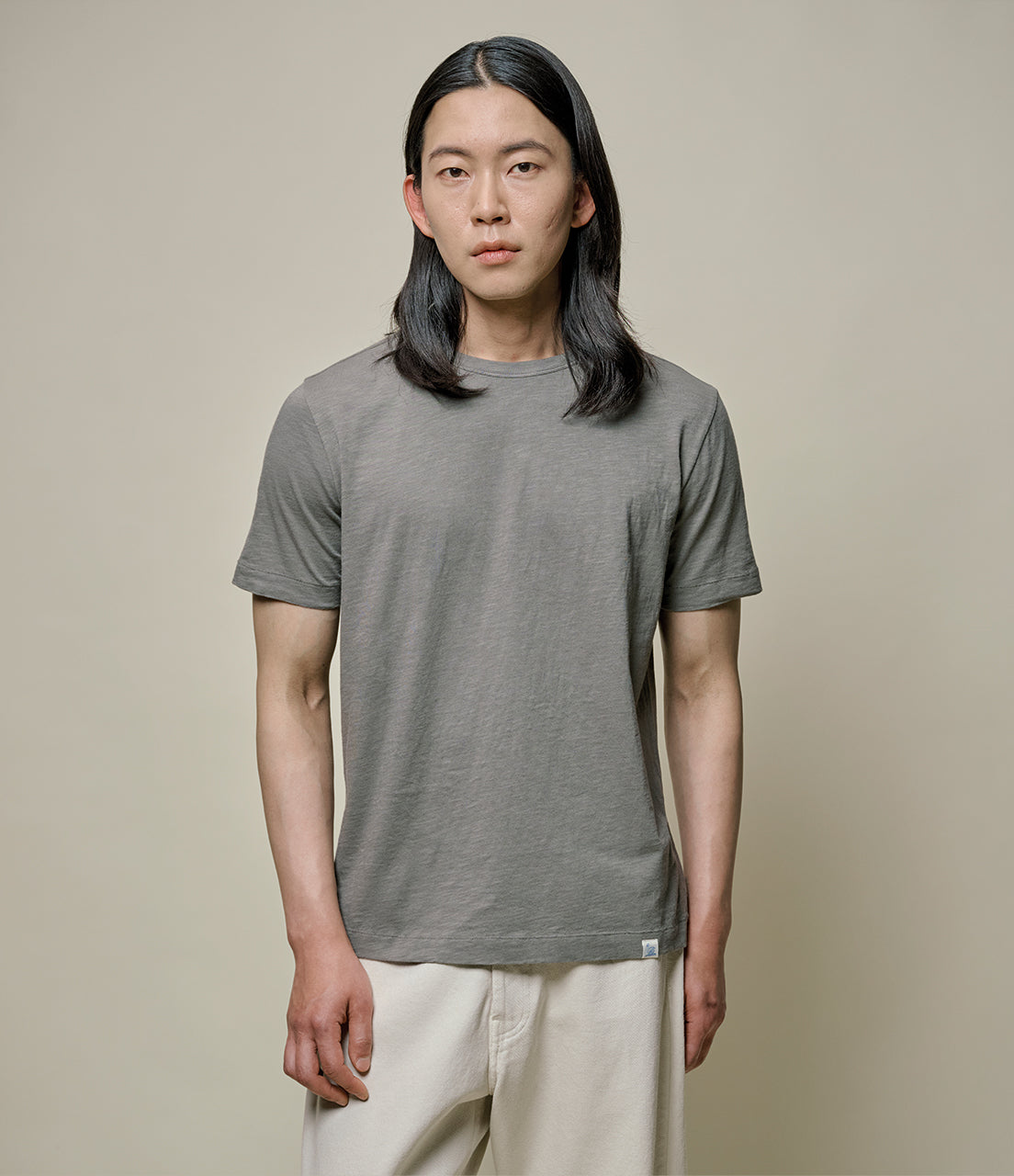 Person wearing a green t-shirt and white pants against a beige background
