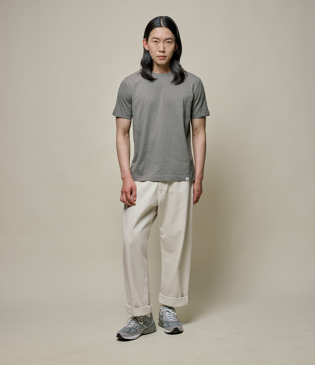 Person wearing a green t-shirt and beige pants against a plain background