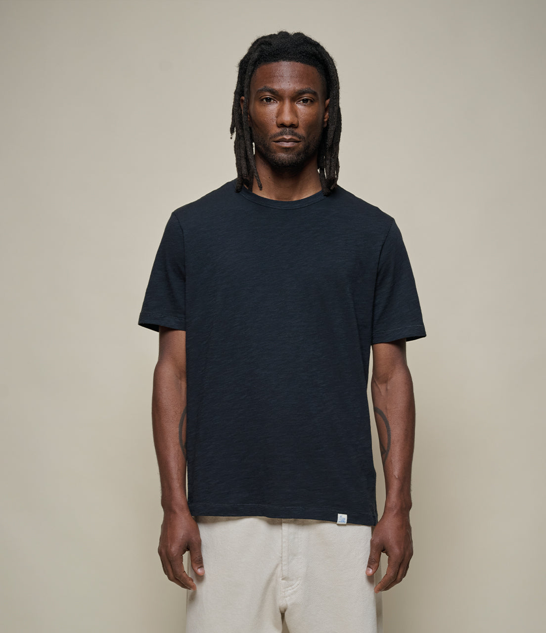 Man wearing a black t-shirt and white pants against a beige background