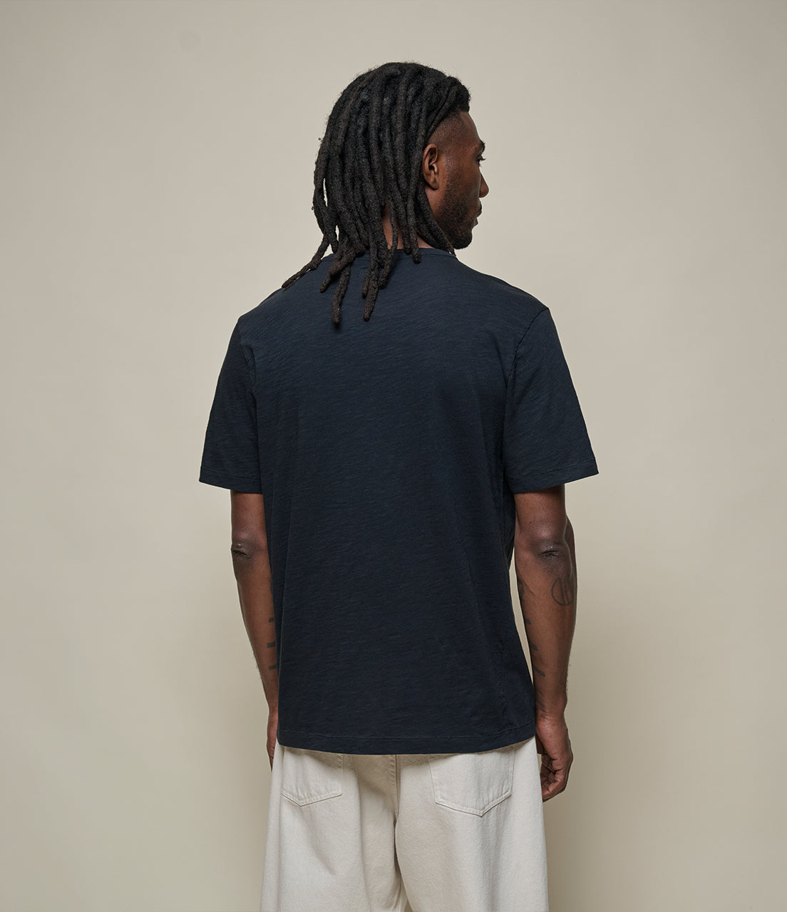 Person wearing a black t-shirt and light-colored pants against a beige background