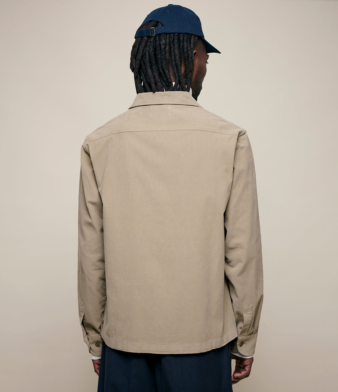 Person wearing a beige corduroy shirt and blue cap on a plain background