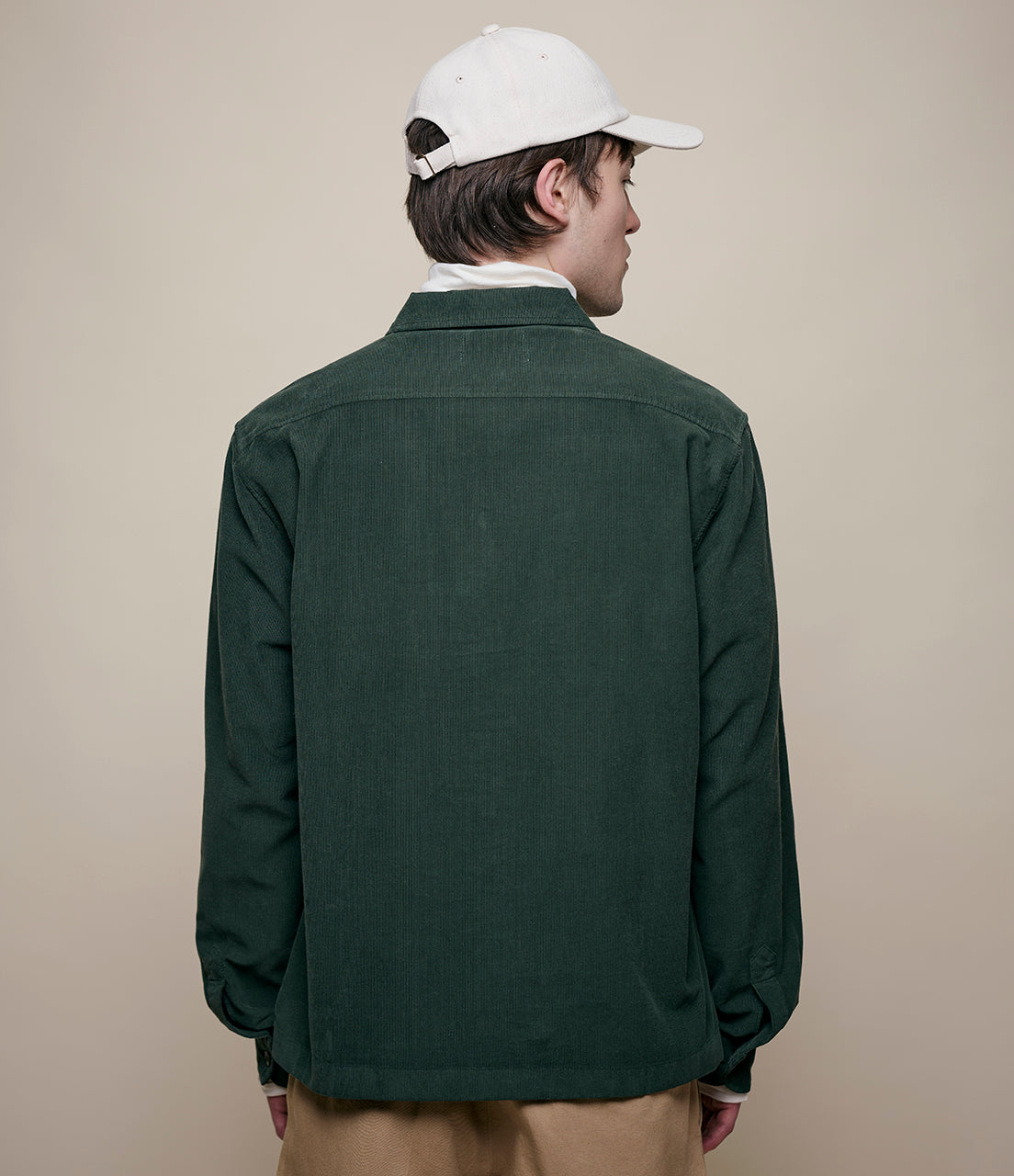 Person wearing a green corduroy shirt and white cap on a beige background