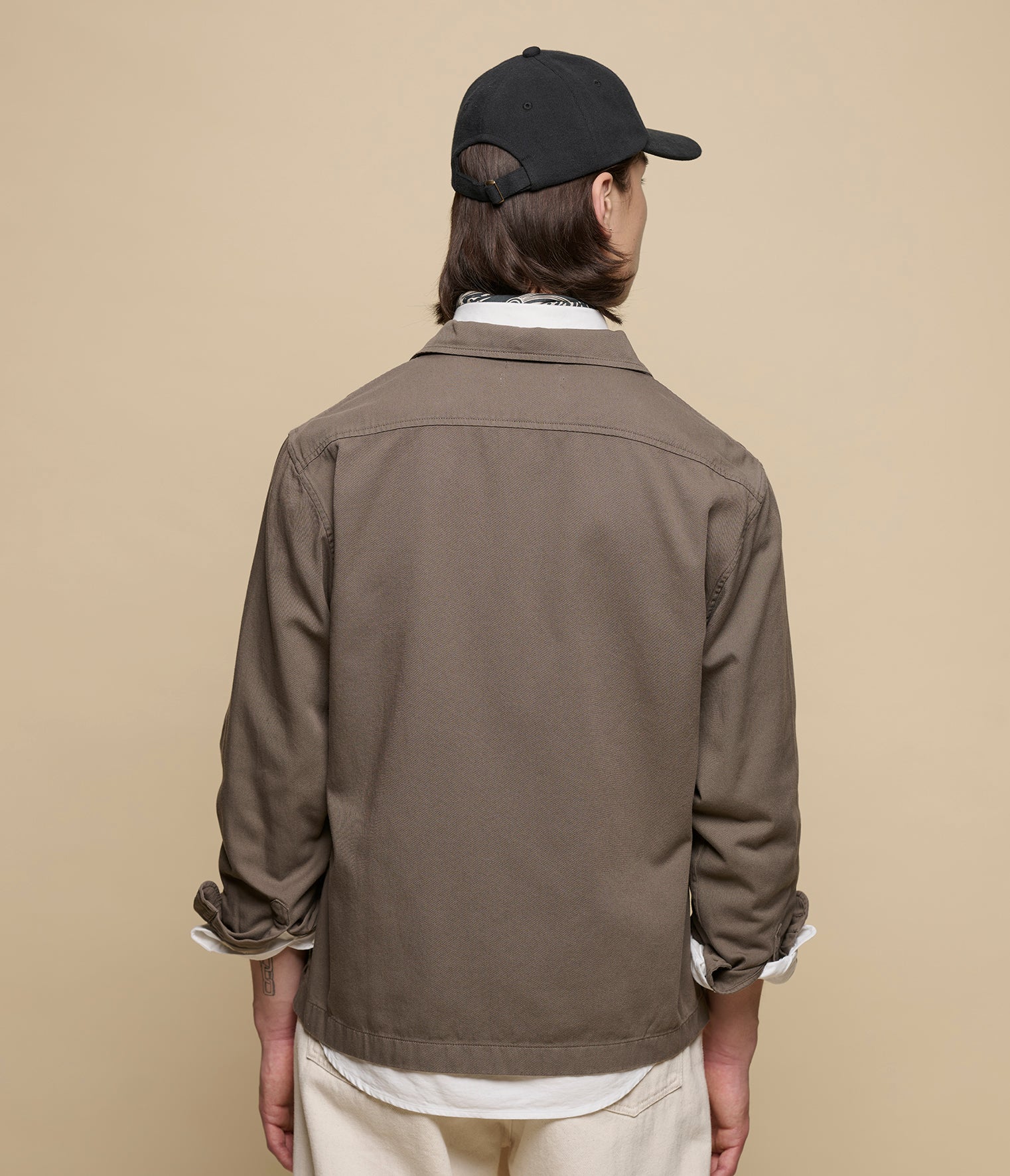 Person wearing a brown jacket and black cap on a beige background