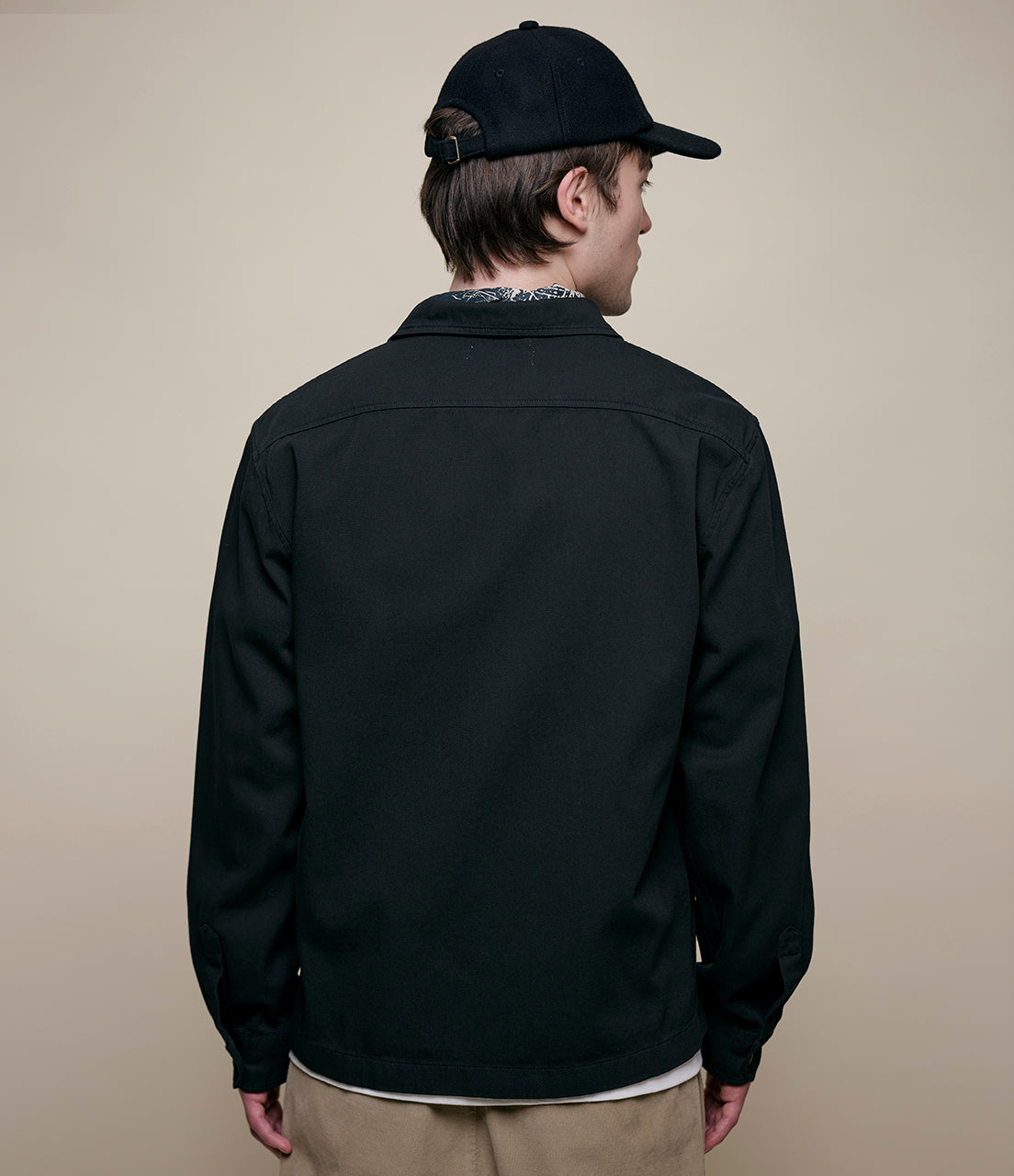 Person wearing a black jacket and cap on a beige background