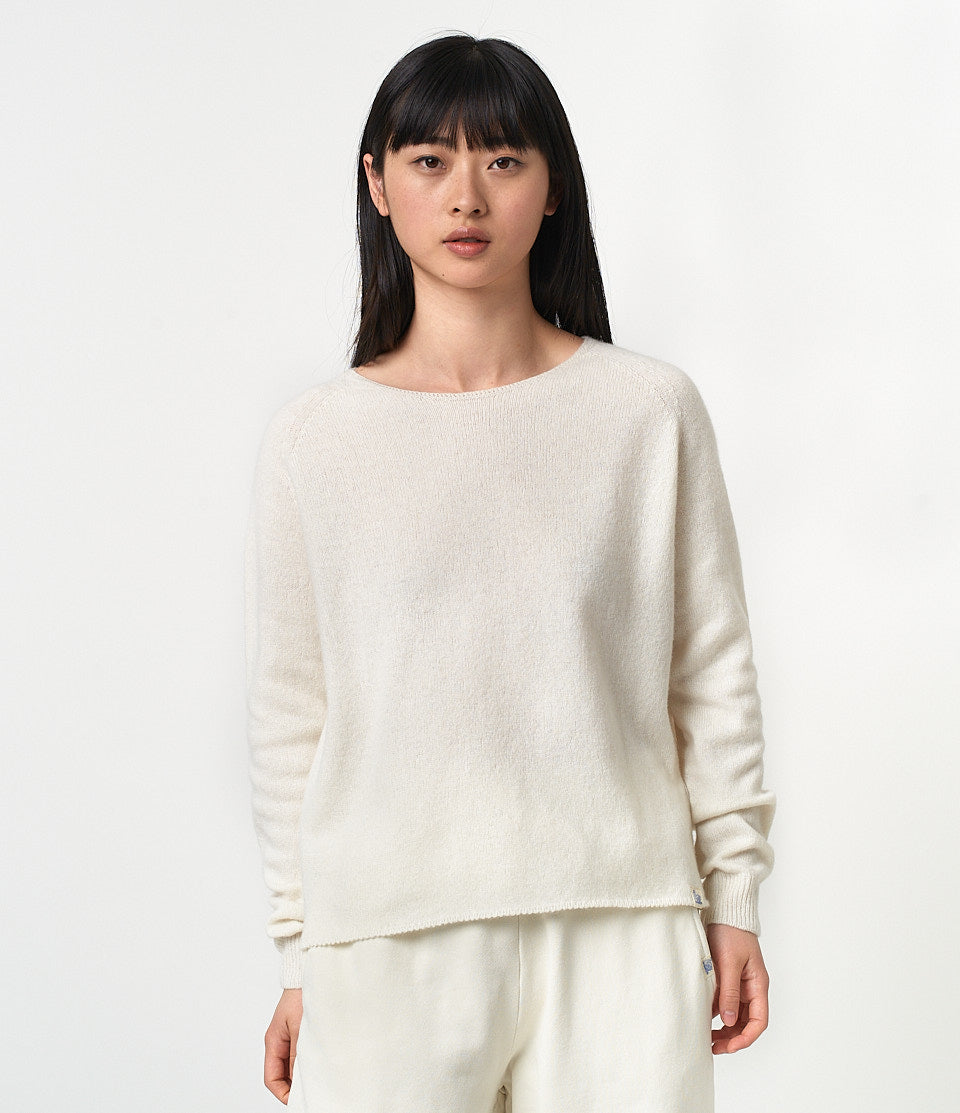 A female model wearing a beige long-sleeved merino wool-cashmere-silk blend raglan sweater with a round neckline.