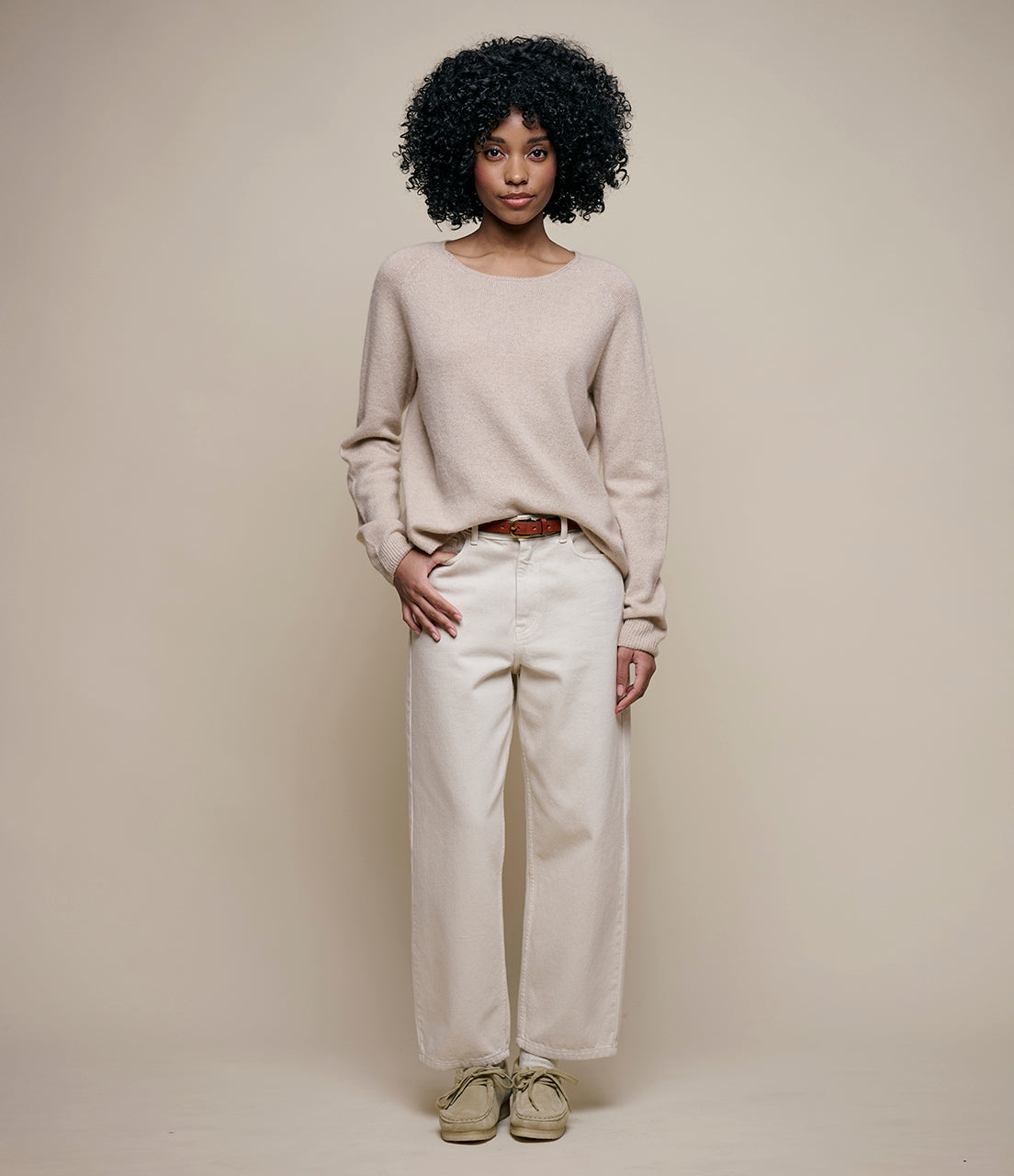 Person wearing a light gray sweater and white pants against a plain background
