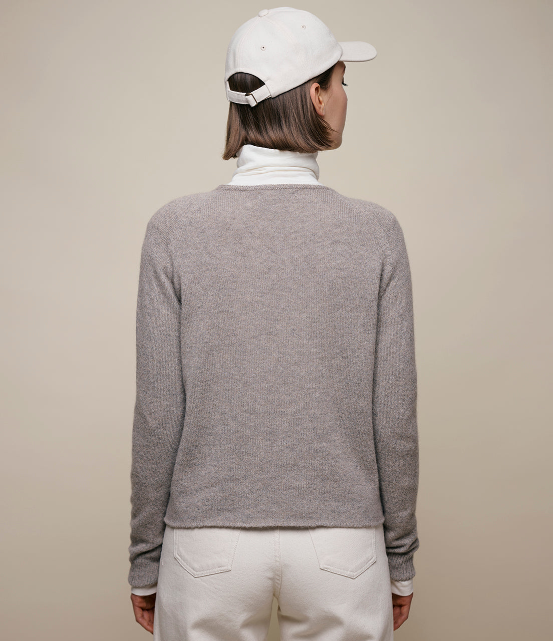 Person wearing a gray sweater and white cap on a beige background