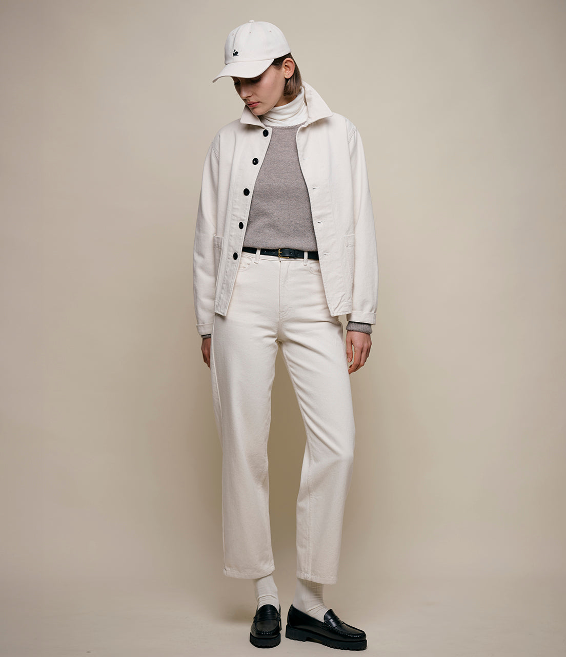 Person wearing a white jacket, white pants, and black shoes on a beige background