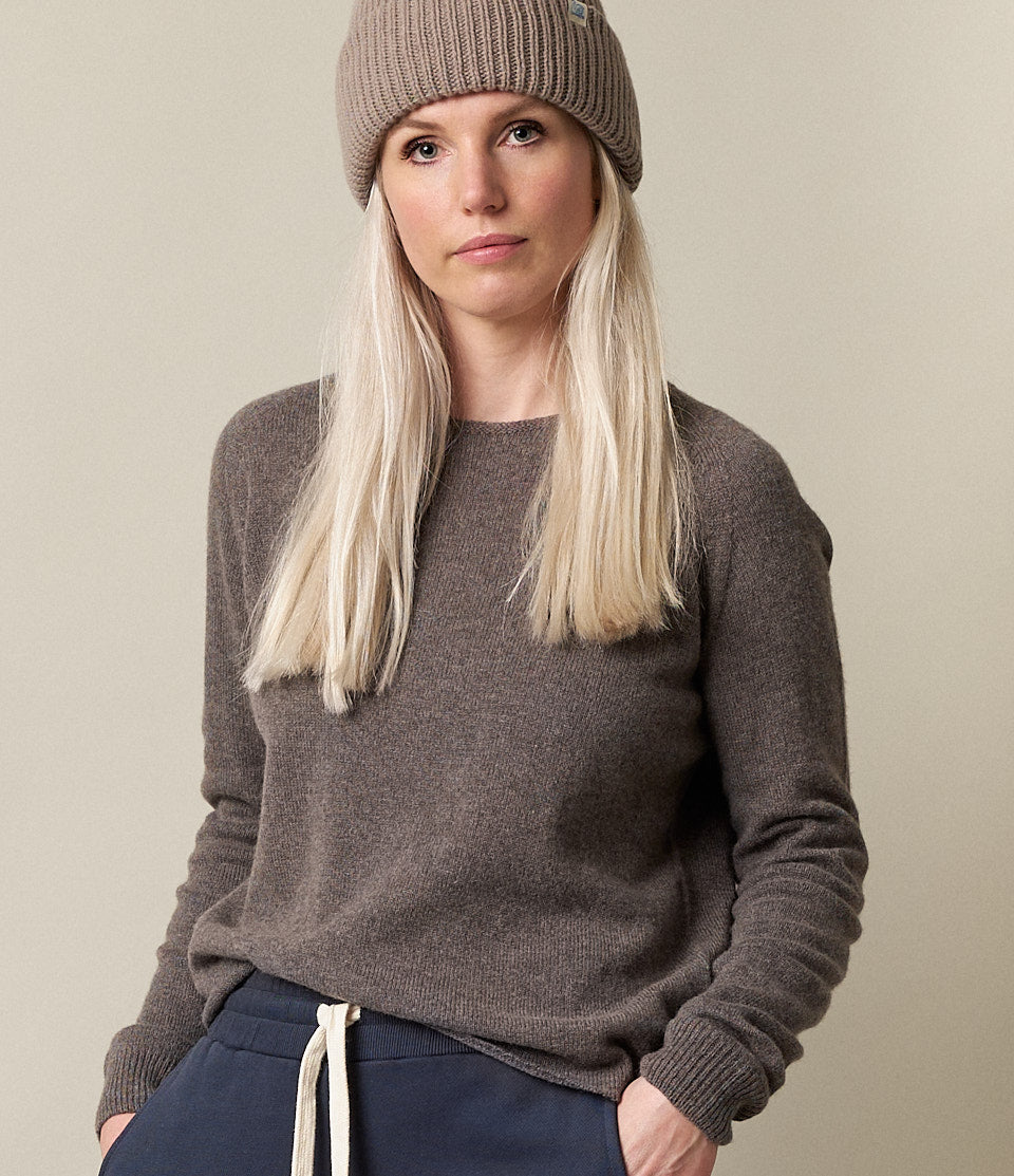 A person wearing a brown long-sleeve pullover with a round neckline, paired with a beanie hat in a matching color.