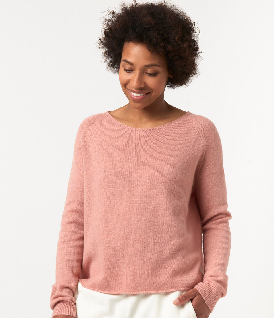 A person wearing a pink, long-sleeved, round-neck Merino Wool-Cashmere-Silk Raglan Sweater paired with white pants.