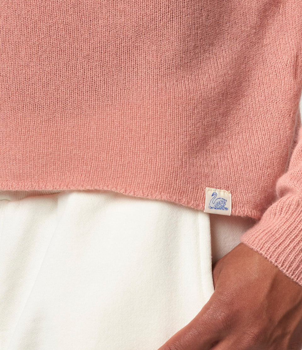 Close-up of a pink sweater with a label against a white background.