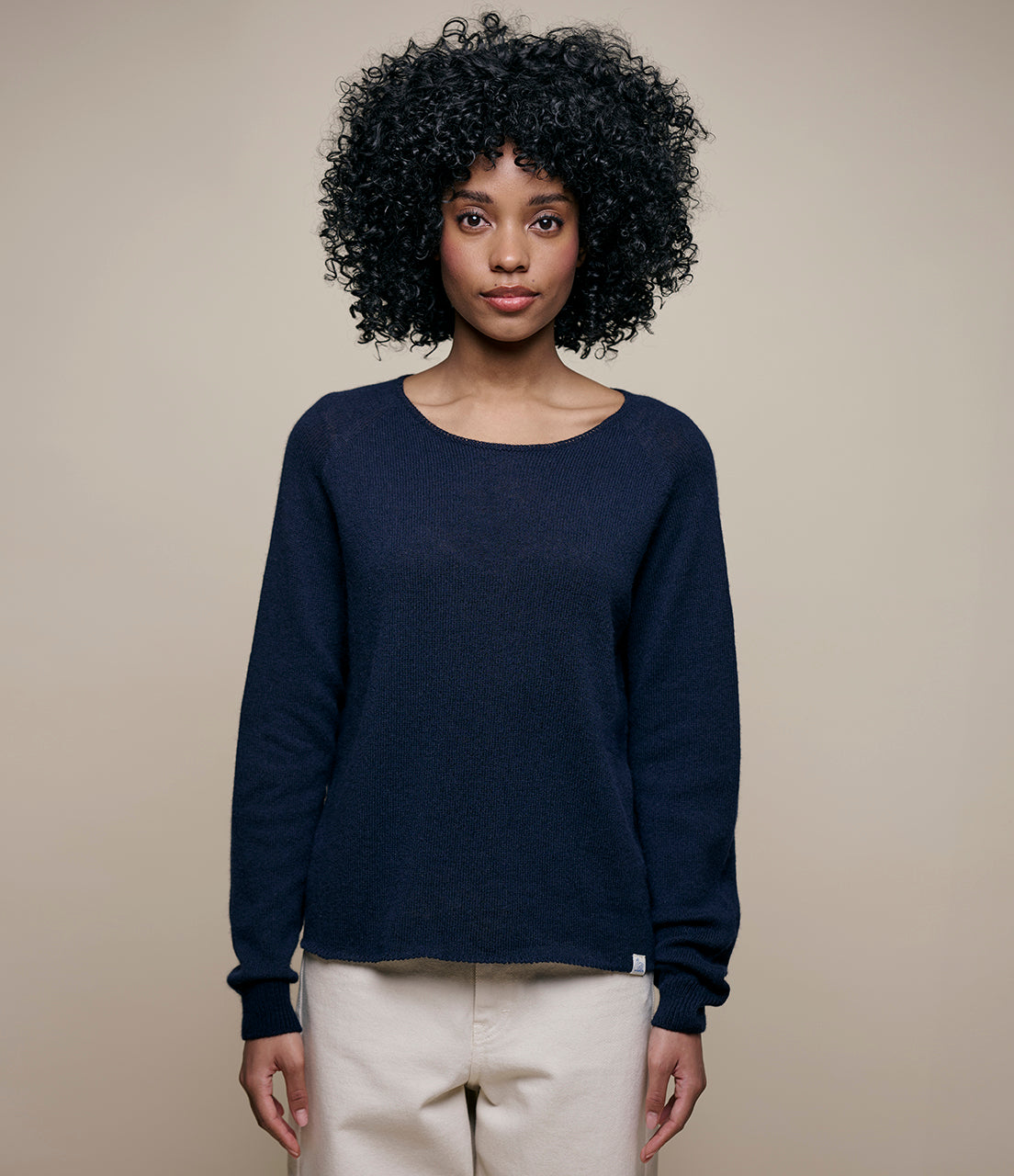 A person with curly hair wearing a navy blue long-sleeve pullover with a round neckline.